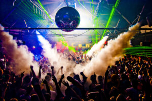 a crowd of ravers dancing inside of a smoke-filled venue
