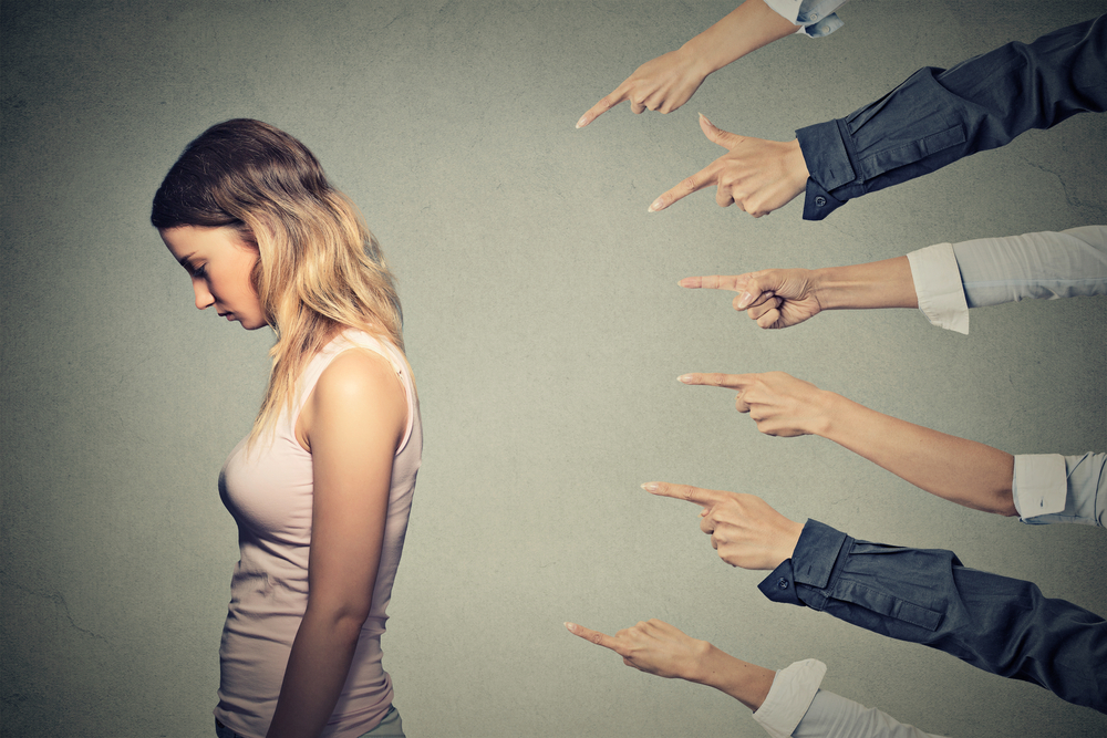 a woman looking down as a group of hands point at her from behind