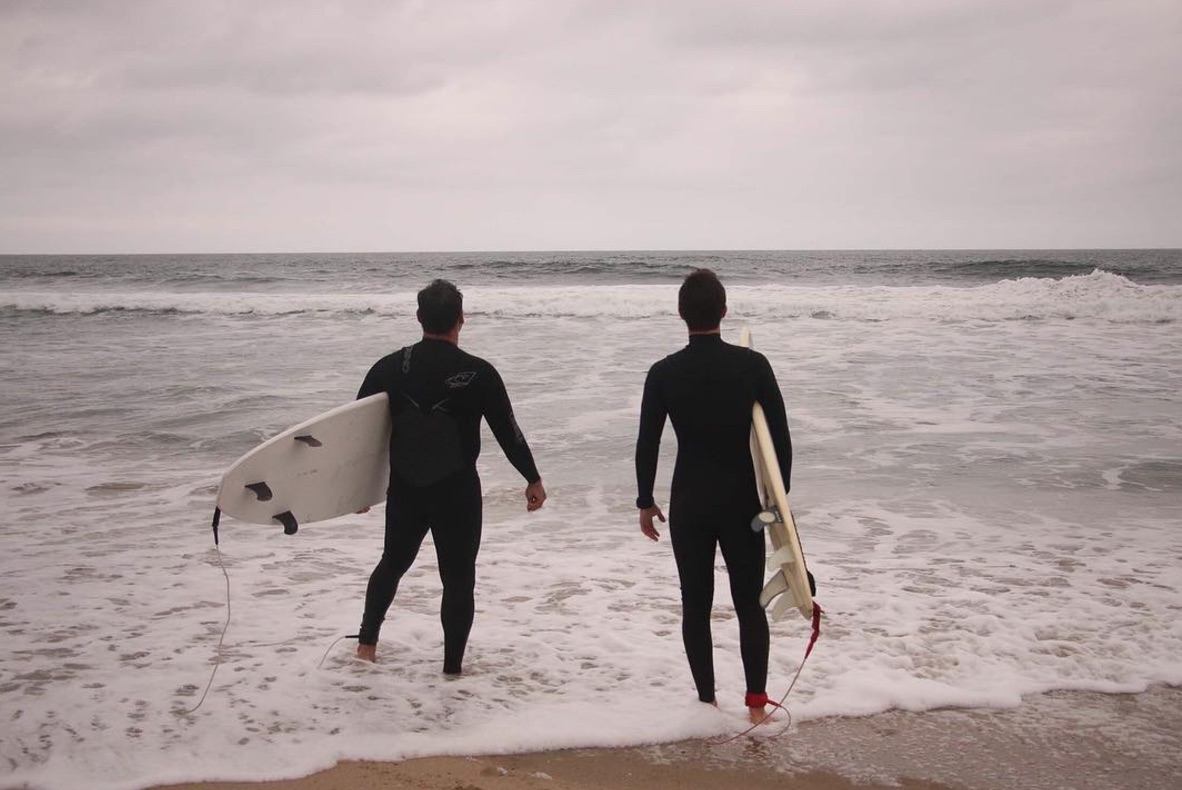 Two men standing at the beach holding surfboards, about to walk into the water