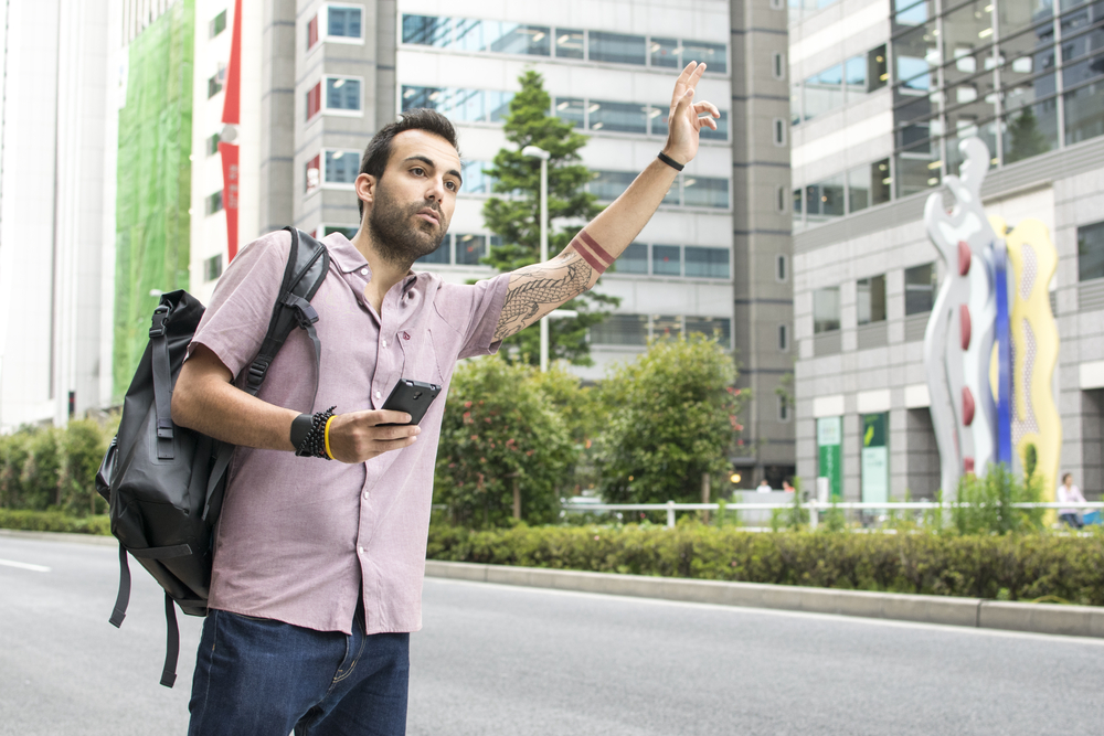 Young man holding cellphone hailing Uber