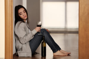Ask an Expert: Is Abstinence the Only Way to Solve My Alcohol Problem? Woman on floor holding glass of wine, looking with concern at bottle of wine.