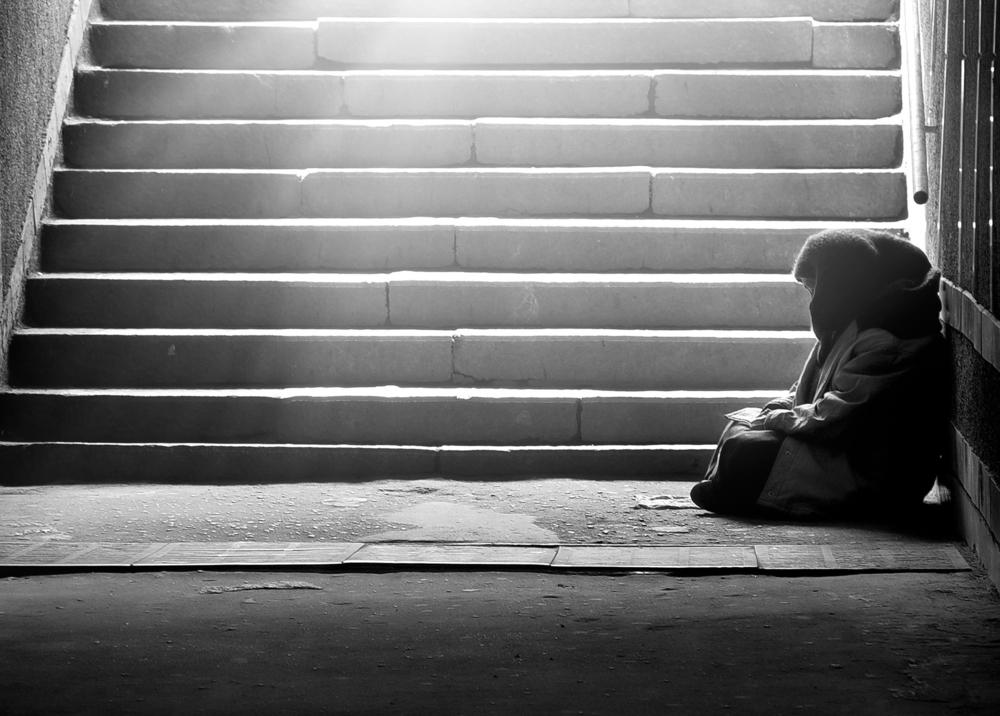 Monochrome photo of homeless woman reading the book in subway under the sunlight