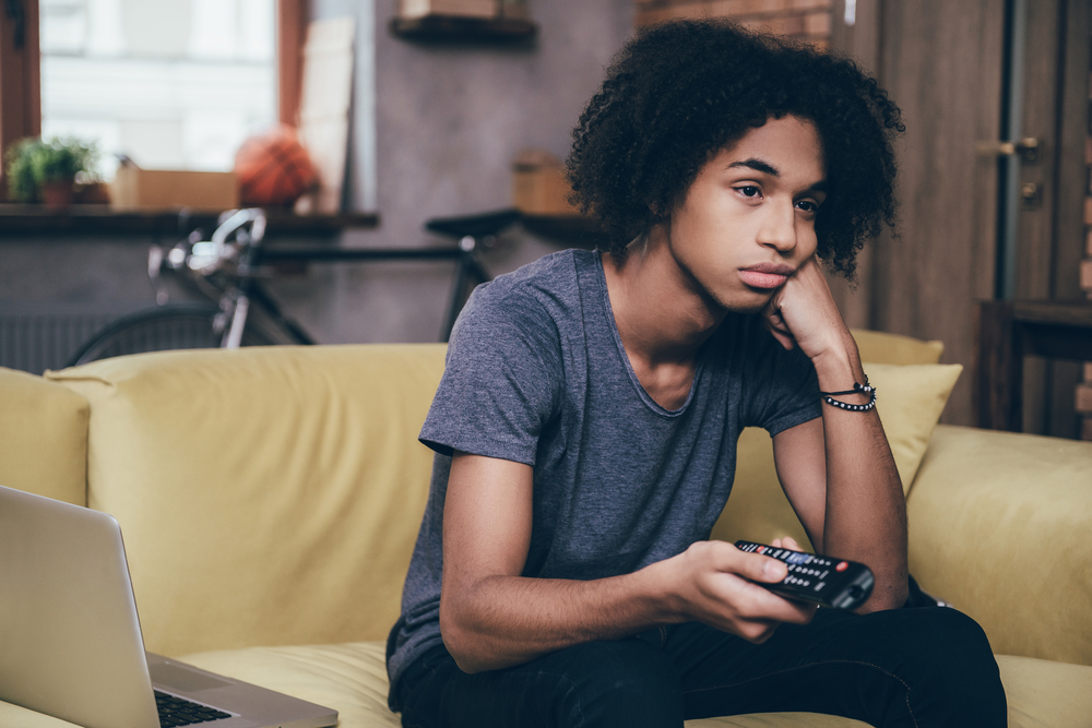 Young man sitting and holding remote, looking defeated.