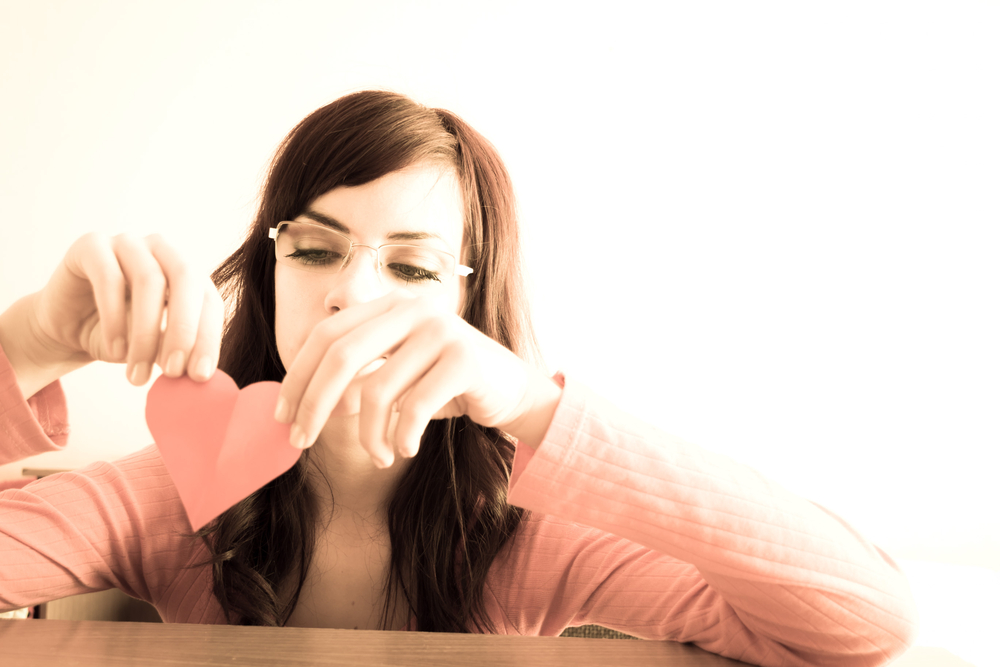 girl ripping up paper heart after break up