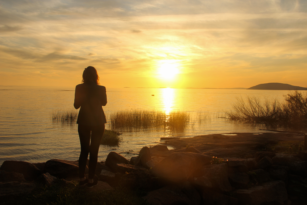 woman standing beside lake at sunset