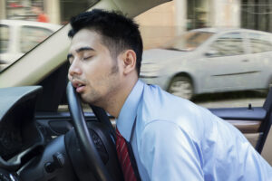 Man sleeping behind the steering wheel of a car.