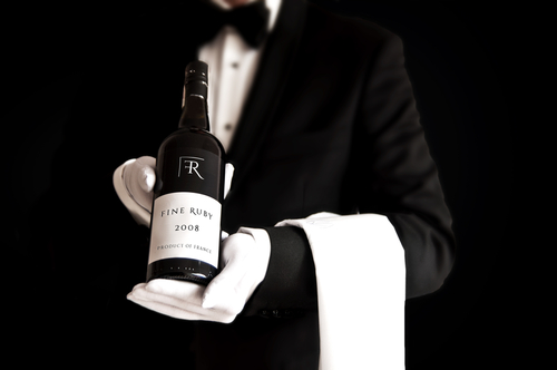 Waiter in tuxedo holding a bottle of red wine with custom designed label