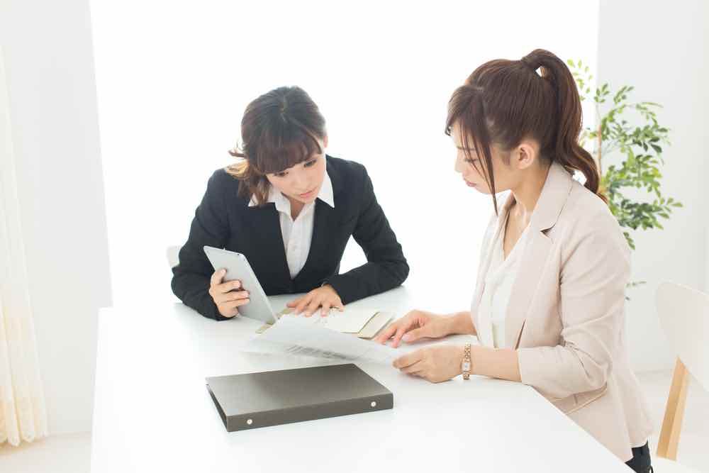 Two women sitting at a table looking at papers and a tablet.