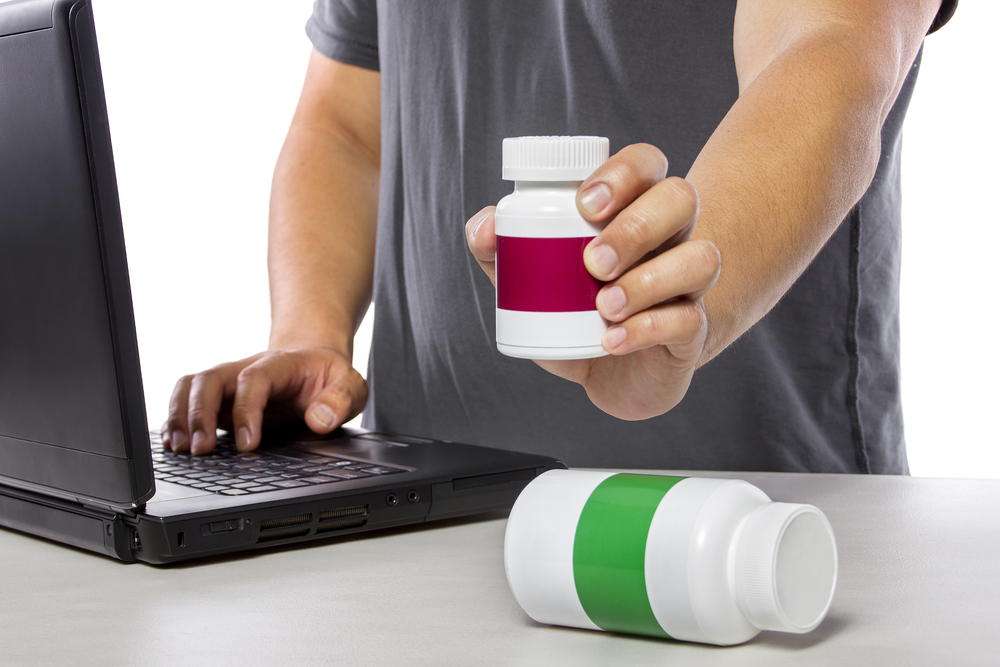 man using a laptop and holding a bottle of pills