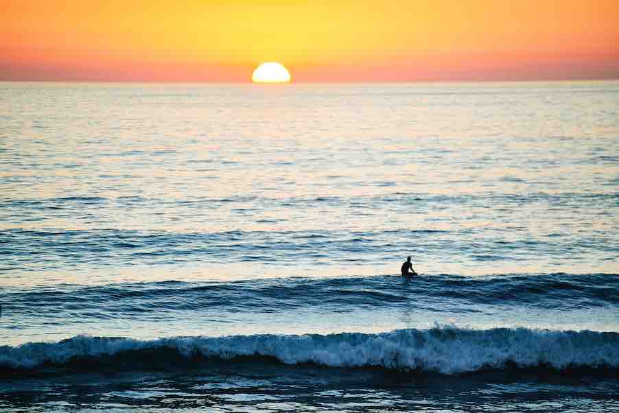 silhouette of person in ocean with sunset.
