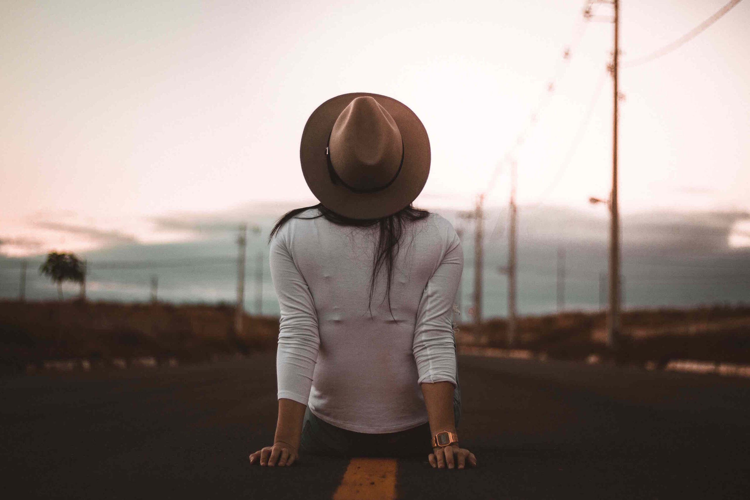 A woman sitting on a road, looking at clouds and sky.