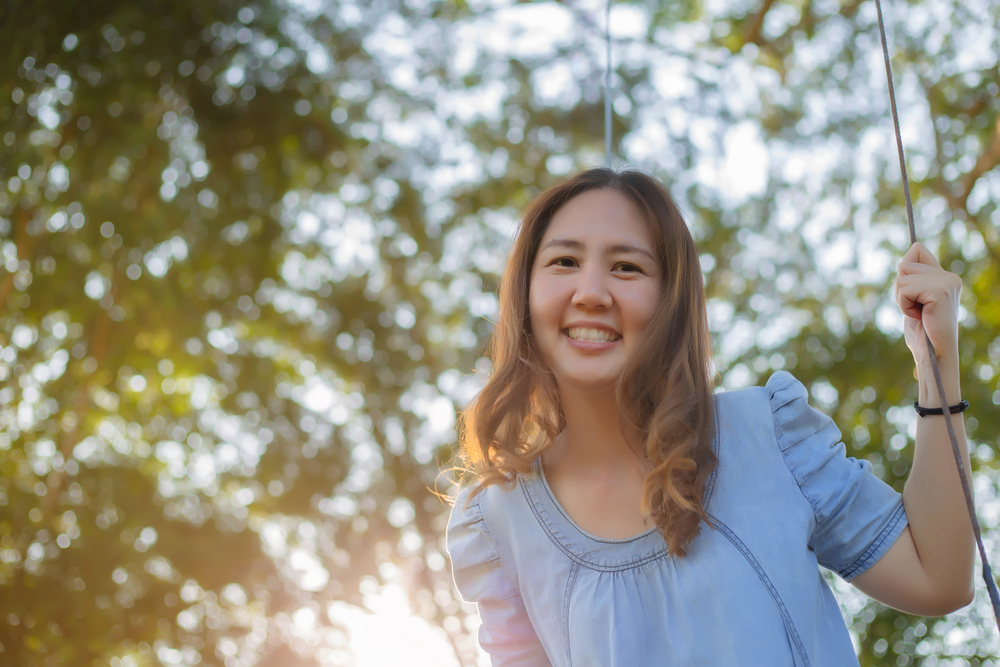 happy woman sitting on a swing under tree canopy