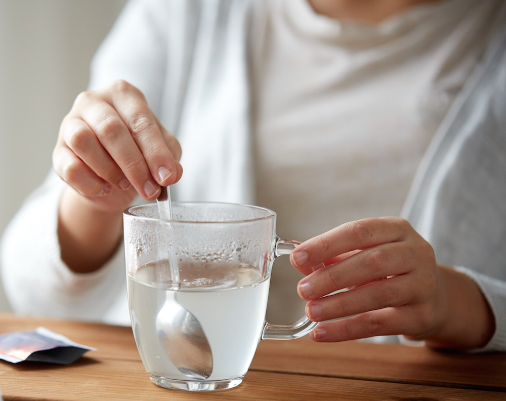 close up of woman stirring medication in cup with spoon and paper tissue on wooden table