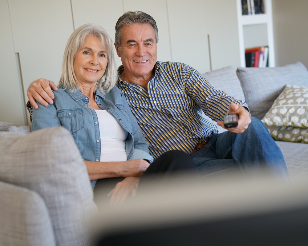 A senior couple sitting on the couch watching TV
