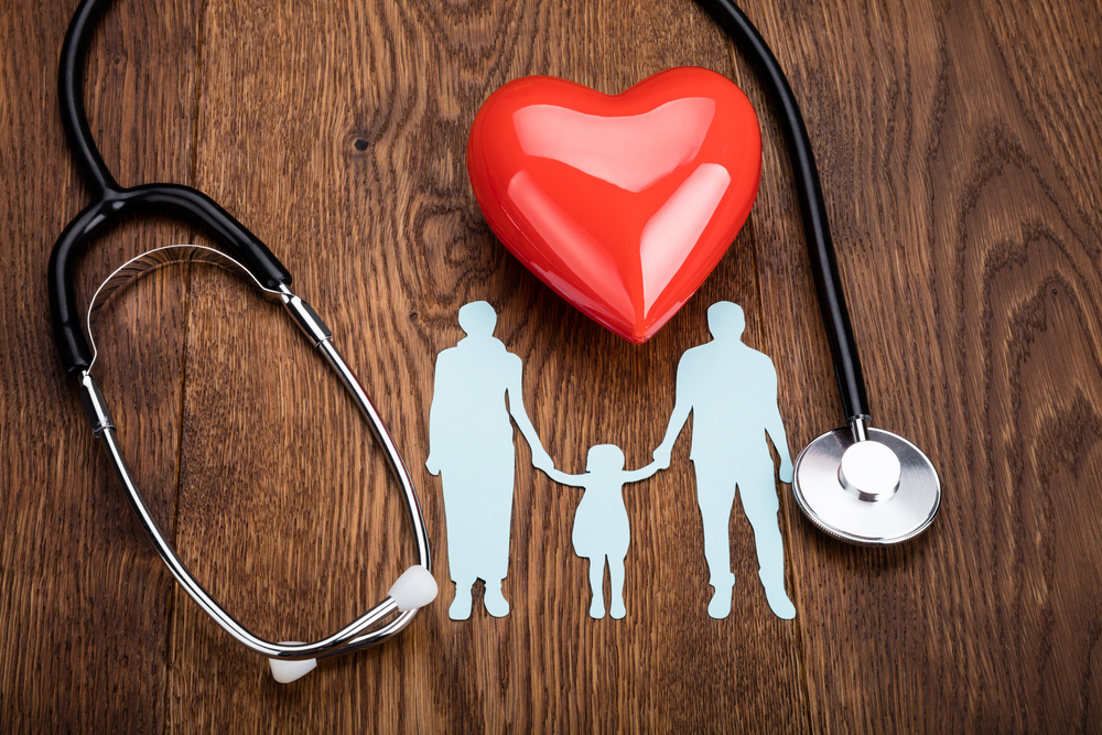 a paper cut out of a small family surrounded by a toy heart and a stethoscope