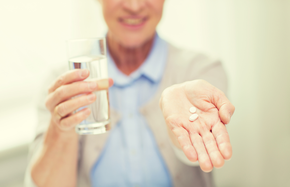 Woman holding pills in one hand and glass of water in the other.