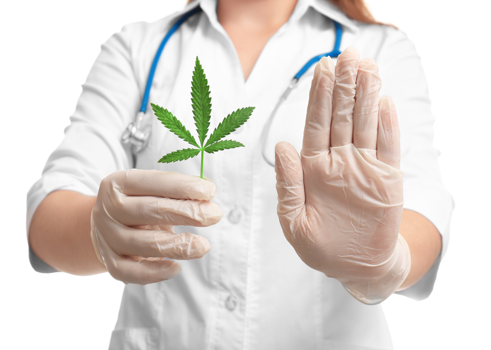 female doctor holding marijuana leaf and holding hand out in stop gesture