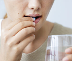 woman placing pill near mouth and holding glass of water