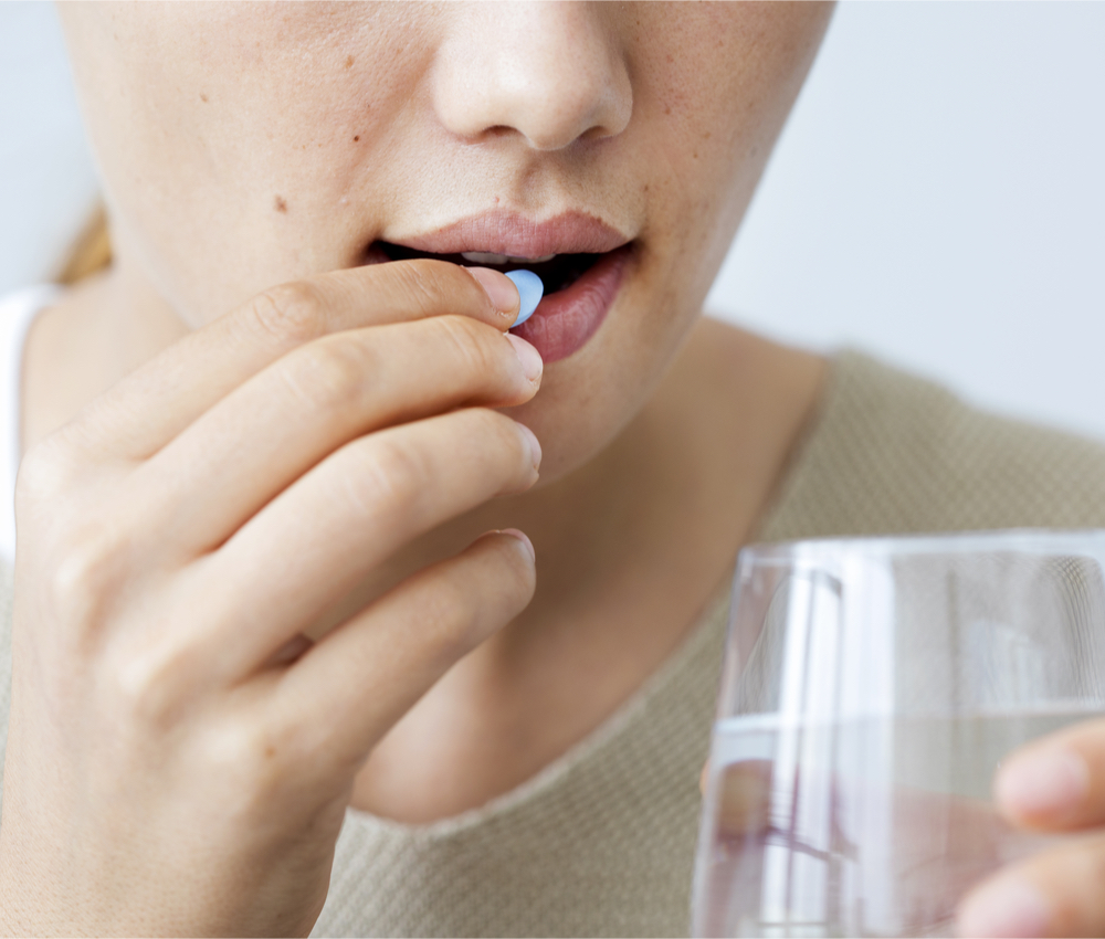 woman placing pill near mouth and holding glass of water