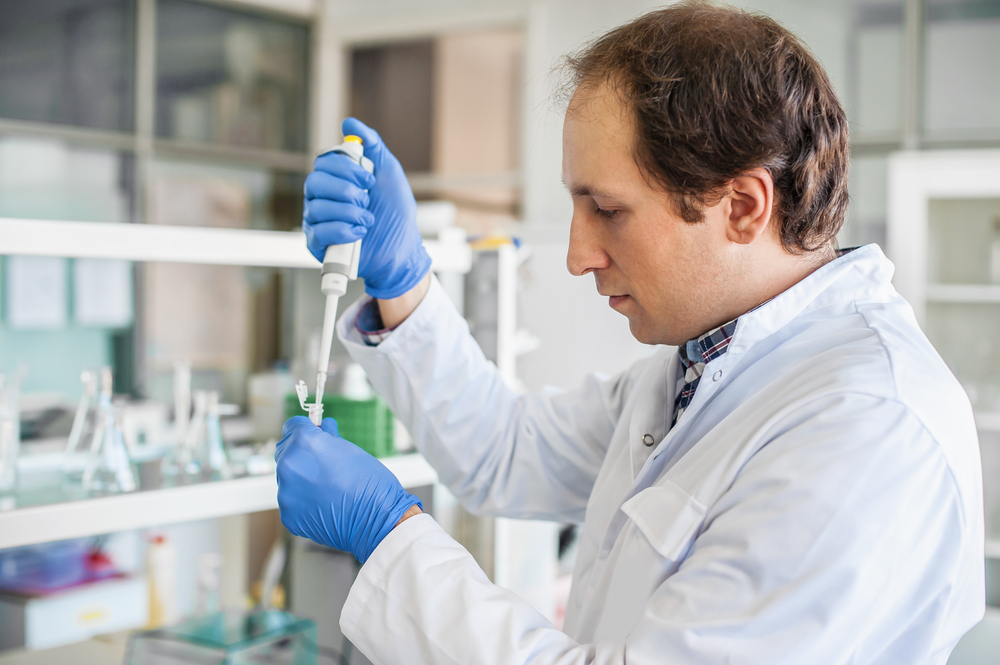 Male scientist in the medical laboratory filling test tubes with pipette.