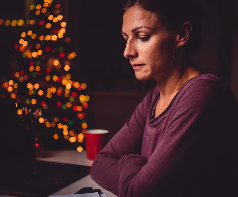 A woman sitting at a table, looking serious, with holiday lights in the background
