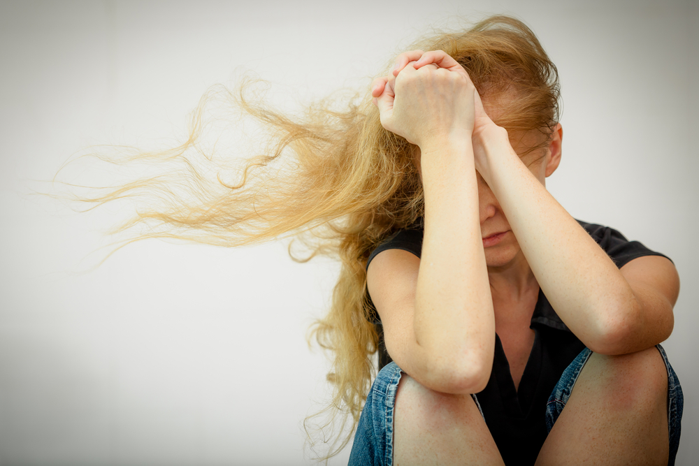 woman sitting with elbows on knees and hands covering face