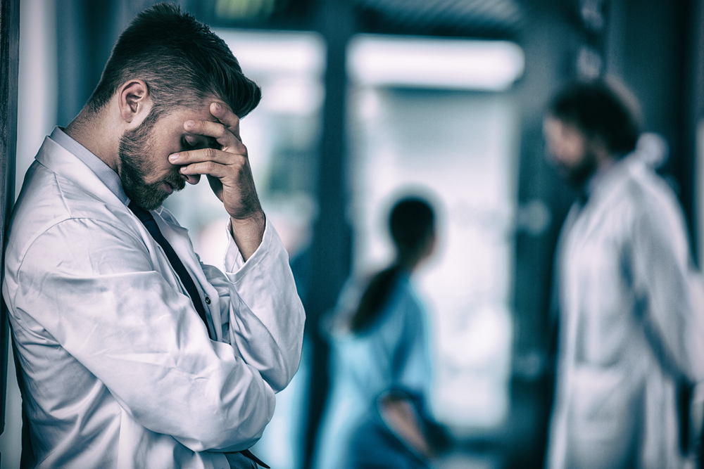 Side view of a stressed doctor standing against wall in hospital