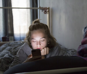 teenage girl checking her phone while in bed