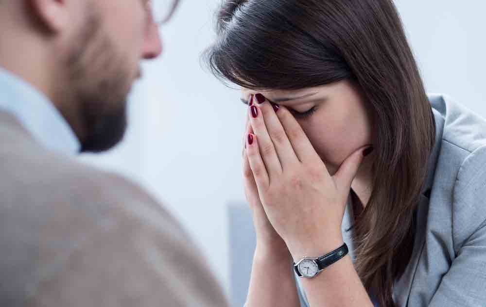 A woman with head in hands, sitting with a therapist