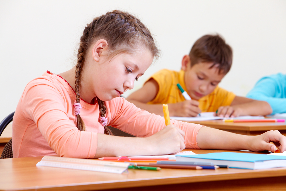 Young girl drawing with schoolboy in background