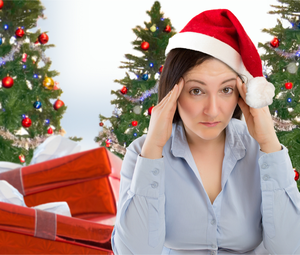 stressed-out woman wearing a santa hat surrounded by Christmas presents