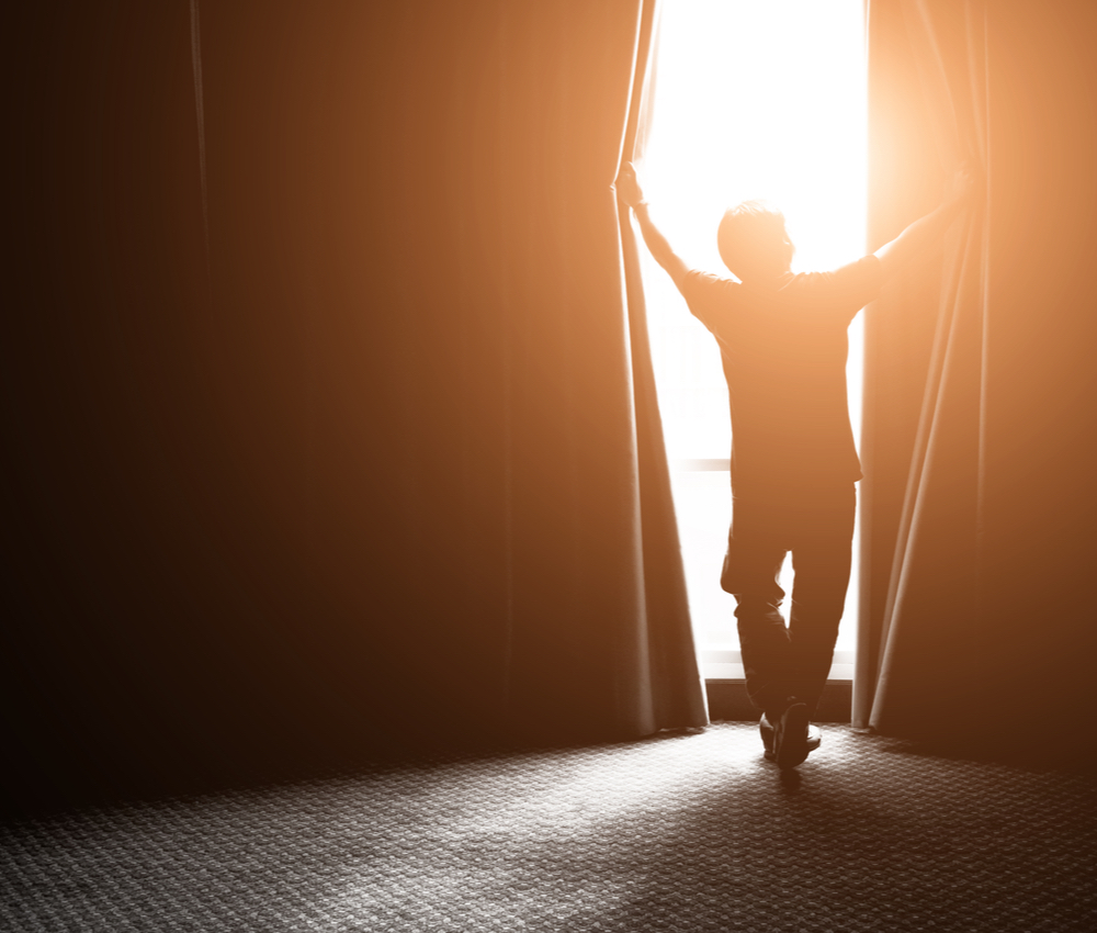 man opening curtain and letting sunshine in.