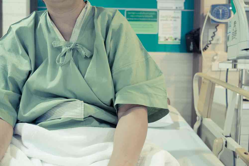 Someone in a hospital gown and bed, only showing torso and arms.