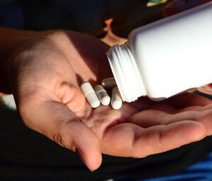 person pouring white pills out of a bottle and into their hand