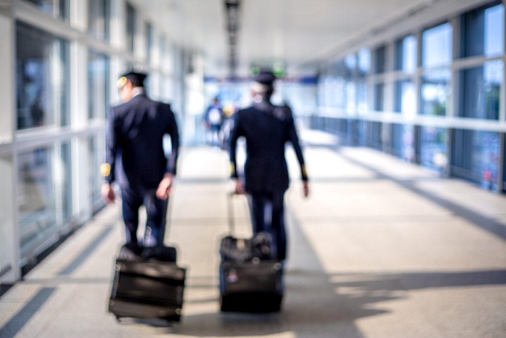 Two pilots wheeling their luggage away in the airport.