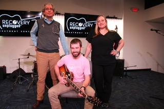 3 people in a music studio, one holds a guitar