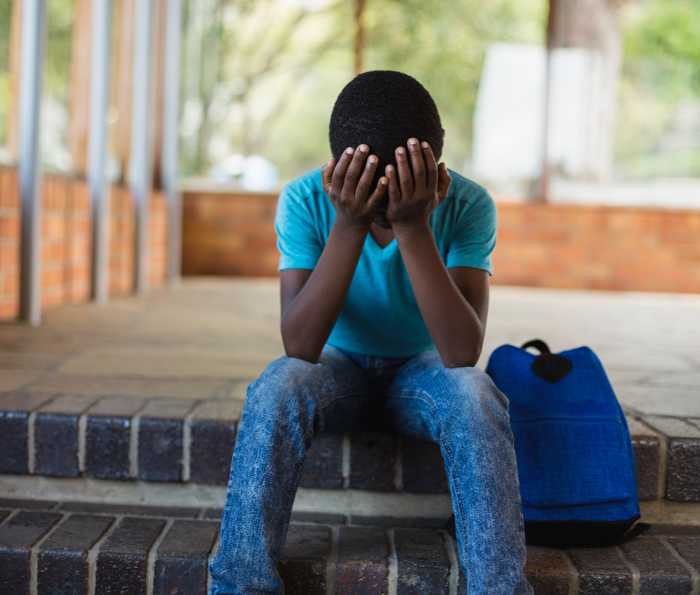 sad school-aged child sitting on step with head in his hands.