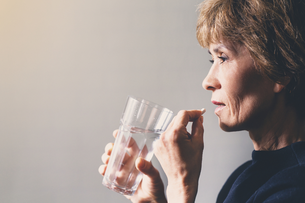 woman holding pill and glass of water