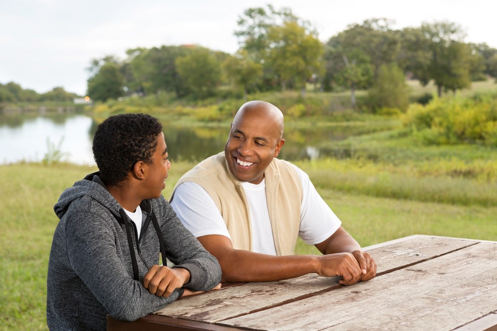A father and son sit at a picnic table, talking