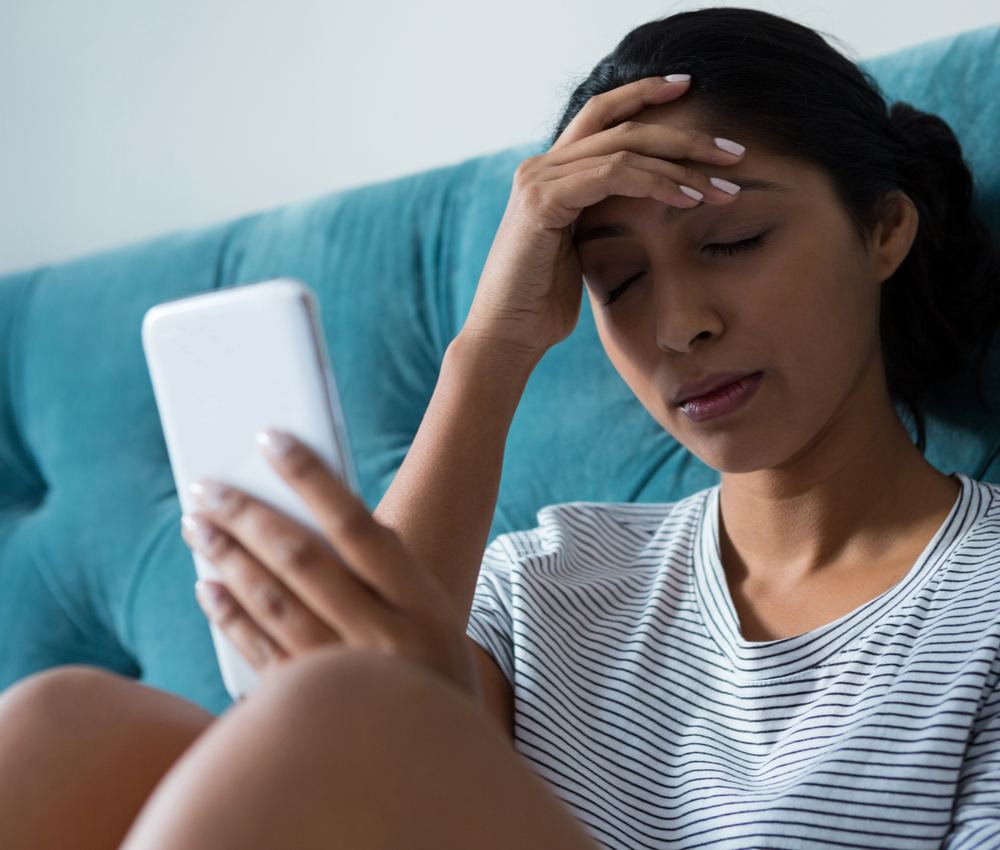 Sad young woman holding mobile phone in bedroom at home