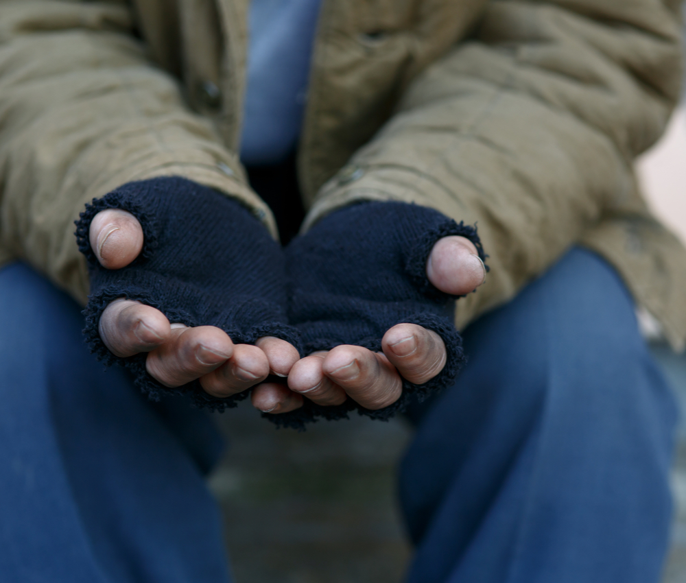 a man with cutoff gloves holding hands out for help.