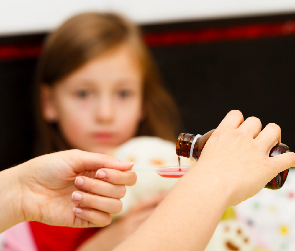 Mother pouring cough syrup onto a spoon as small child watches