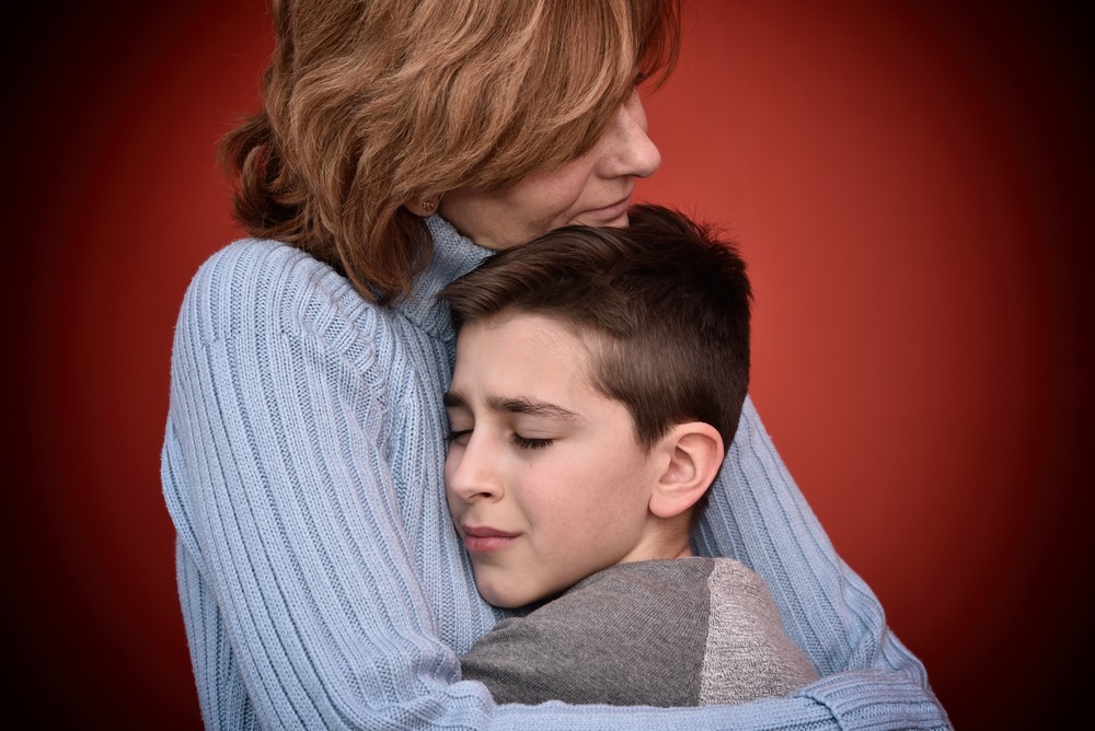 A mother hugging her son, who looks sad or serious.