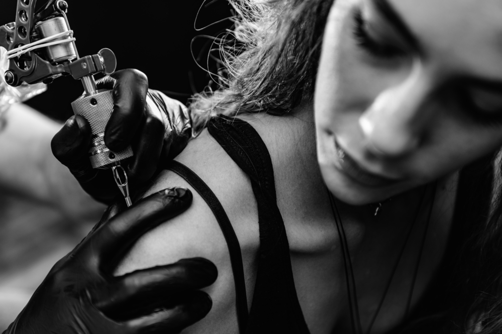 black and white image of woman getting upper arm tattoo