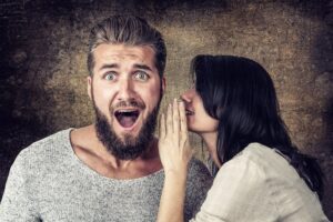 A woman telling a man a secret. He is surprised.