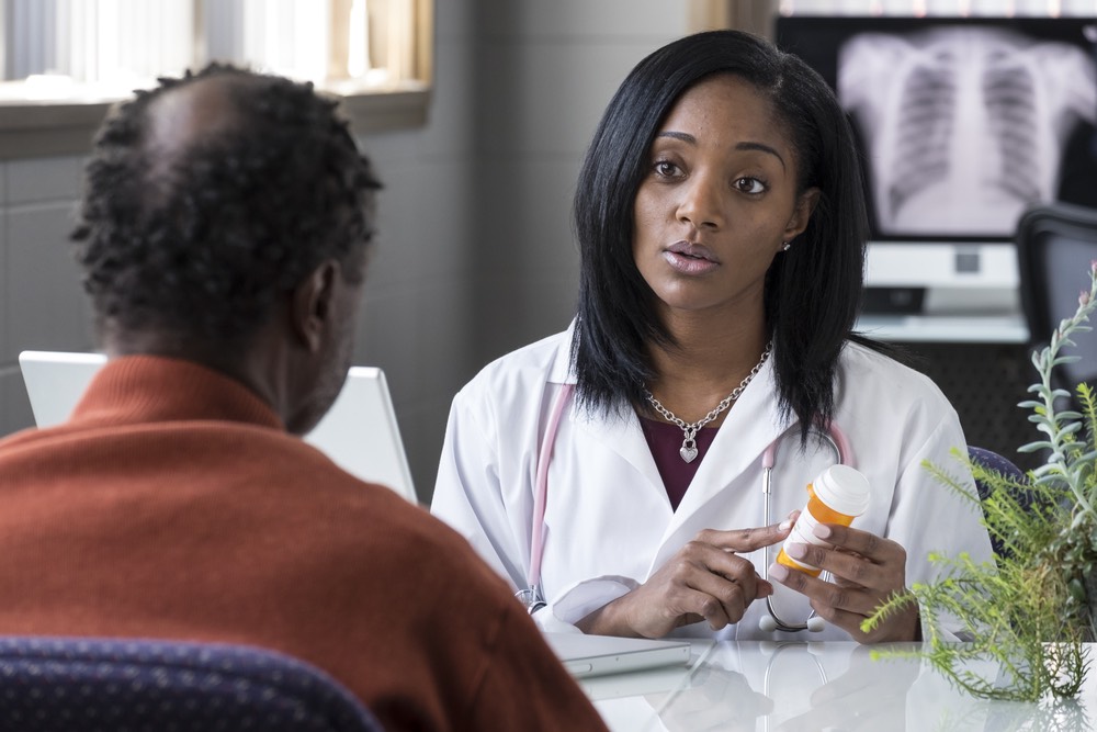 A doctor holding a pill bottle and talking to a patient.