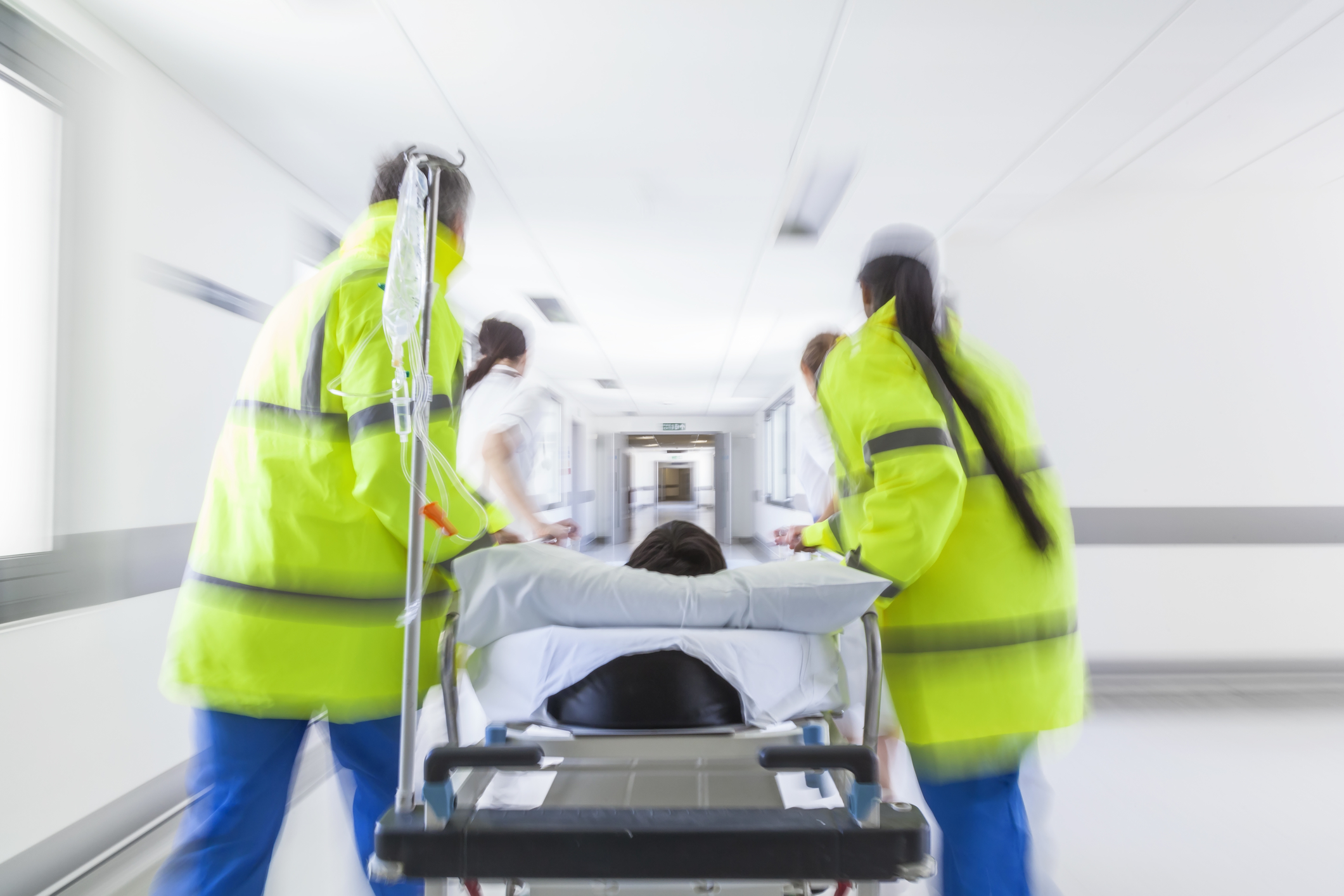 A motion blurred photograph of a patient on stretcher or gurney being pushed at speed through a hospital corridor by doctors & nurses to an emergency room