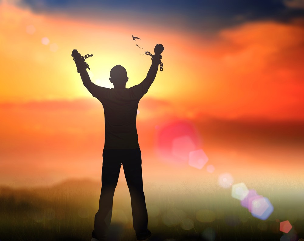 silhouette of man breaking out of handcuffs and raising his hands in front of a sunset