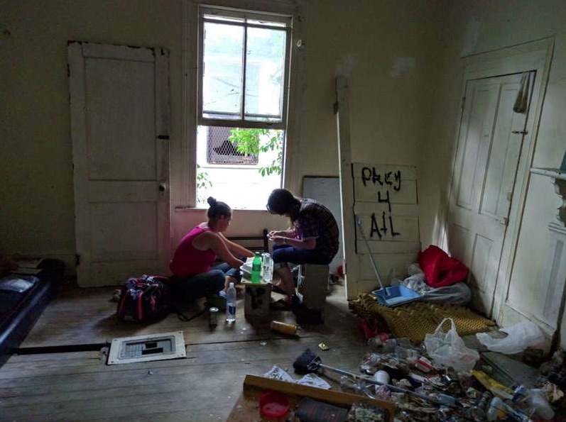 Two people preparing heroin by a window in a rundown apartment