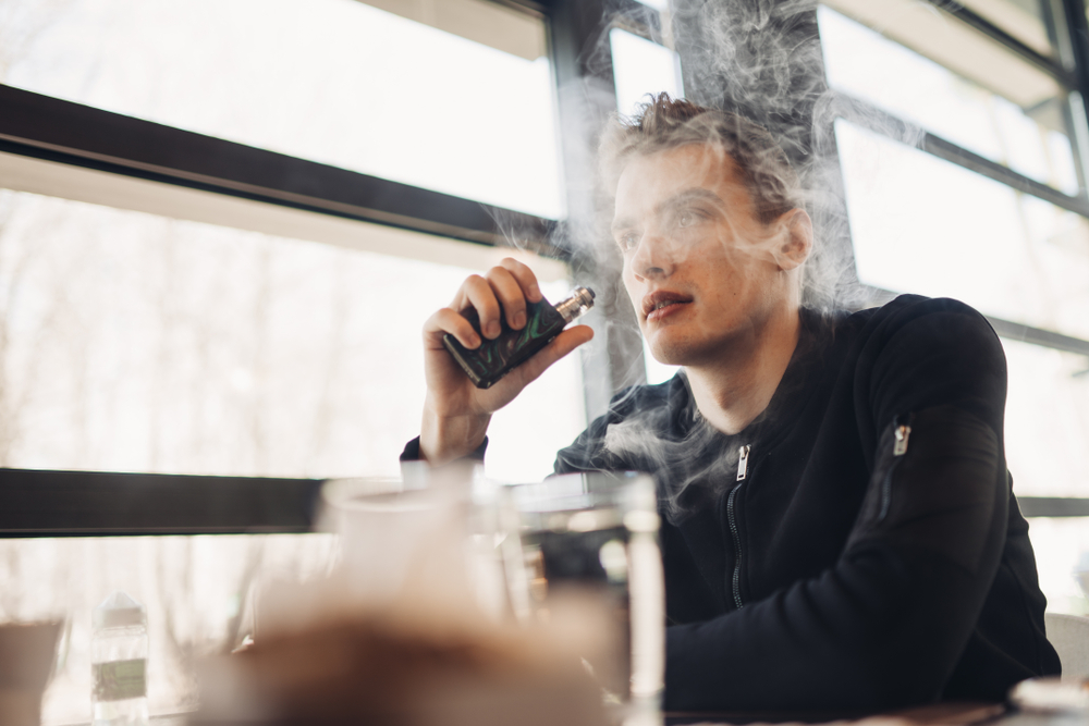 man sitting in public space using his vape.
